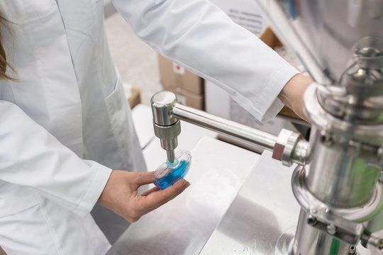 Side view close-up of the hand of a female technician filling a plastic container with liquid substance, for laboratory tests during quality control in a cosmetics factory