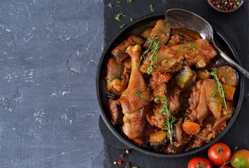 Chicken stewed with vegetables and tomato on a stone board in a frying pan.