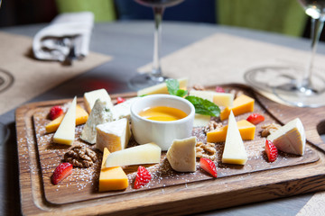 various cheeses with nuts and berries on a wooden Board