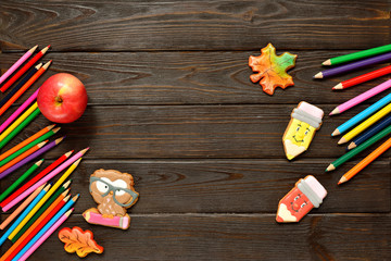 Back to school concept background with colored pencils, red appple and gingerbread on wooden table