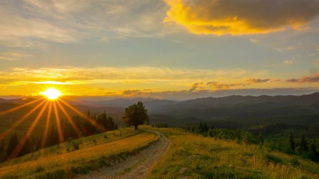 Sunset Sky in the Mountains with a Lone Tree and Dirt Road in the Foreground and Clouds in the Background. Timelapse. 4K.