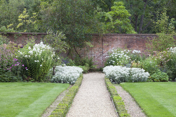 Stone path leading to a brick wall between white flowers in a cottage English garden, on a summer...
