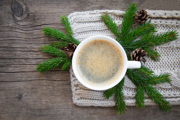 a cup of hot coffee with foam and Christmas tree standing  on a wooden christmas holiday rustic table  background wrapped in warm knit wool scarf. view from the top. space for text.concept of heat.