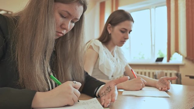 Two schoolgirls use cheat sheets on an important exam.