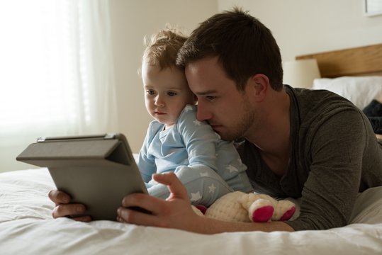 Man showing tablet computer to daughter while lying on bed