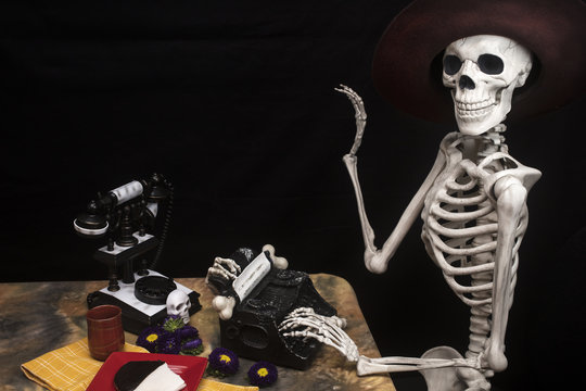 Halloween Skeleton At a Table with Typewriter, Phone and Cookies