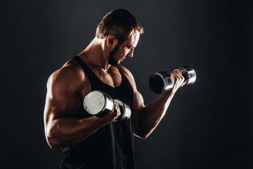 Strong athletic bodybuilder doing exercises with dumbbell,  six pack, perfect abs, shoulders, biceps, and triceps  chest, personal fitness trainer flexing his muscles