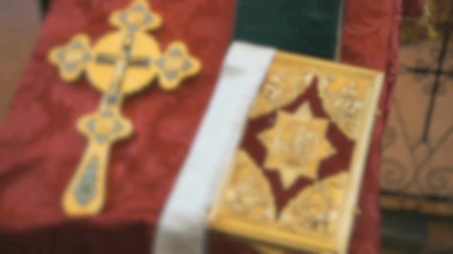 Blurred video. The large gold Orthodox cross and the Bible in a Golden frame lying on the table with Burgundy fabric in the Orthodox Church. Close up