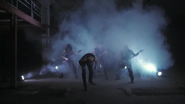 A musical rock band stands in smoke in a dark room.