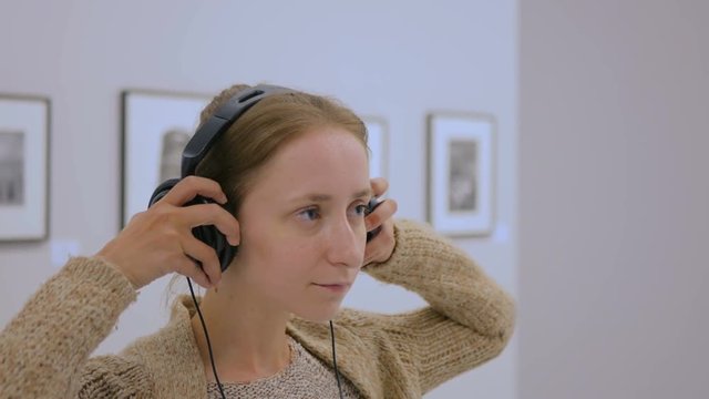 Woman looking at exposition, using headphones and listening audio guide in modern photo gallery. Education and entertainment concept