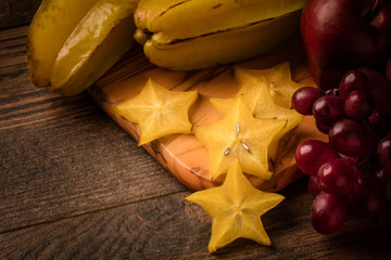 Star fruit on wooden table with grapes, apple, and pomegranate