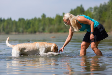 pretty woman plays with a labrador dog in a lake