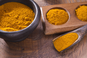 Turmeric powder in bowl and spoon on wooden table (curcuma longa)