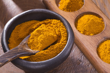 Turmeric powder in bowl and spoon on wooden table (curcuma longa)