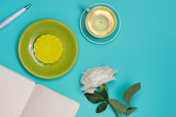 Snow skin mooncake and tea cup with flowers on dark background. Open notebook with copy-space.