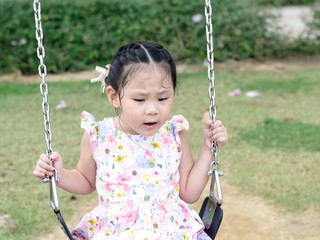 Adorable girl having fun on a swing in playground.