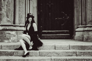 Pretty girl in a vintage style of 20s with feathers. The lady in a long black dress with bright make-up, pale skin near the European Catholic Church. Luxury retro look