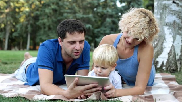 Mom, dad and son with a tablet on the nature. Family with a child and a tablet computer in the park.