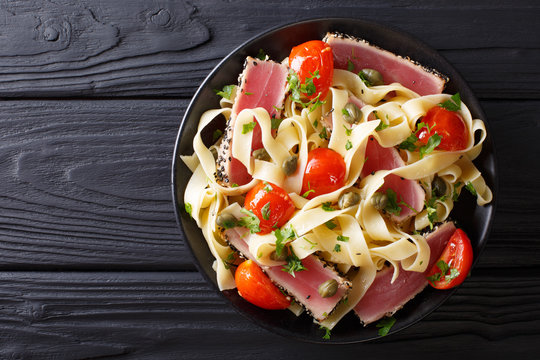 Delicious fettuccine pasta with tuna steak, tomatoes and capers close-up on a plate. Top view horizontal