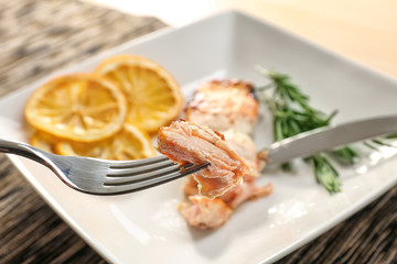 Fork with tasty hot salmon and blurred plate on background