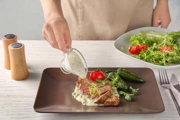 Man adding sauce to sliced steak on brown plate