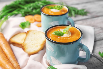 Cups with delicious carrot soup on table