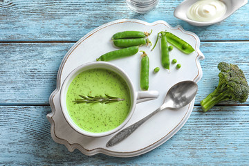 Mug with delicious broccoli soup on white wooden board