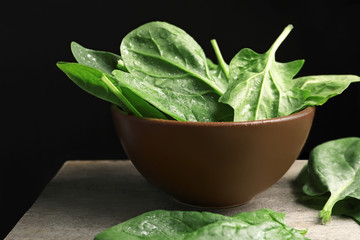 Bowl with fresh spinach leaves on table against black background