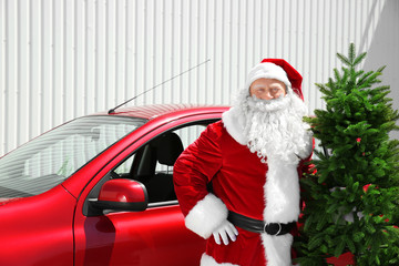 Authentic Santa Claus with Christmas tree standing near red car outdoors