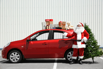 Authentic Santa near red car with gift boxes on it's top and Christmas tree