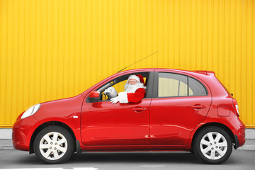 Fototapeta na wymiar Authentic Santa Claus driving his red car, against yellow background