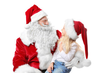 Fototapeta premium Cute little girl in Christmas hat sitting on Santa's lap against white background