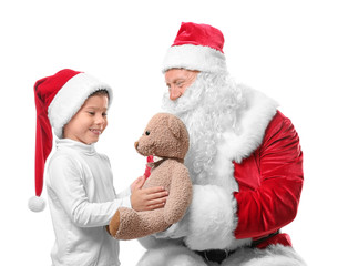 Authentic Santa Claus giving teddy bear to cute boy in Christmas hat on white background