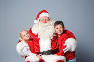 Santa Claus with cute children on color background