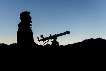 Man silhouette looking at mountain peaks near telescope in summer evening at sunset on mountain outdoor.