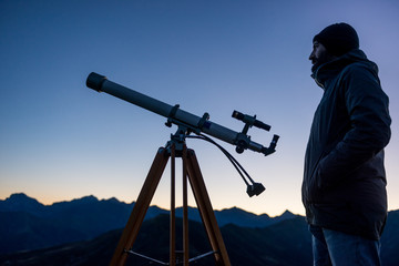 Man looking at mountain peaks near telescope in summer evening at sunset on mountain outdoor.