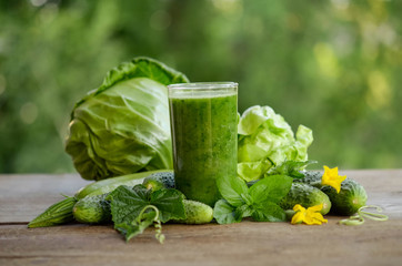  glass with green smoothie on a wooden table and  vegetables with mint leaves