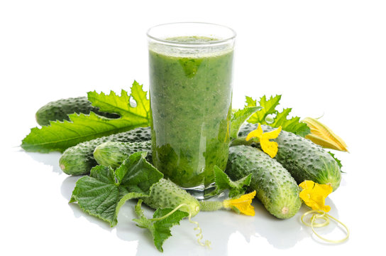 glass with green smoothie and  cucumbers, flowers, leaves isolated on white