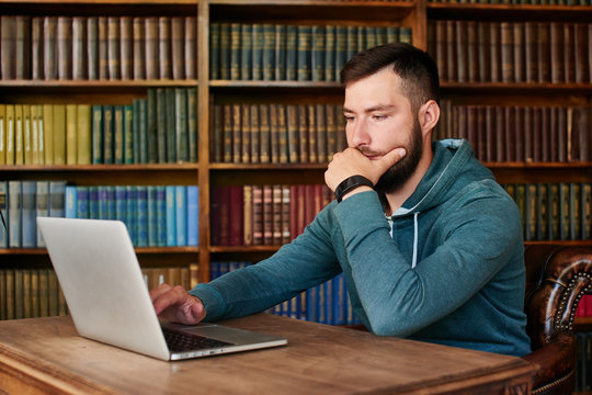 The guy sitting at the table with laptop on background of books
