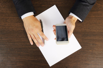 Phone in hands of a businessman on the desktop close-up, top view.