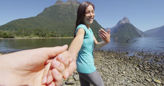 Follow me POV - Couple in love having fun. Boyfriend following girlfriend holding hands in New Zealand outdoors in nature laughing and smiling enjoying active outdoor lifestyle hiking in Milford Sound