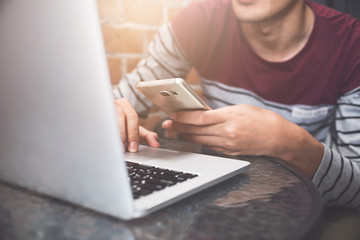 Close up Young man sitting at desk using smartphone andlaptop computer for online shopping