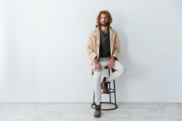 Caucasian young bearded man sitting isolated over grey wall