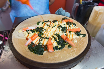 Making vegetable crepe, roll with tomatoes and lettuce. Salty crepe or pancake with fillings made by street vendor's hands at outdoors creperie in Thailand.