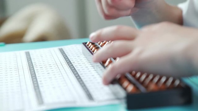 An inquisitive and diligent boy does homework and math. Pupil is healed by mental arithmetic, using special scores. Close-up: children's hands write with a pencil and use accounts of Abakus (Soroban).