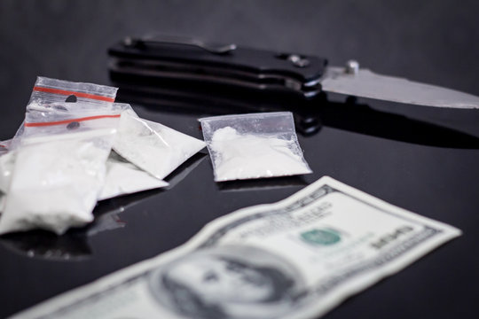 Cocaine in packages, dollars, knife on black background