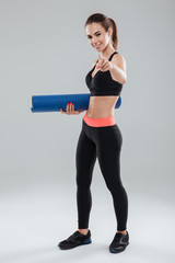 Full length picture of happy fitness woman holding fitness mat