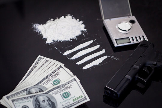 scales with cocaine, many dollars and hand gun on black background