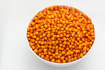White plate filled with berries of sea-buckthorn on a white background. Top view.