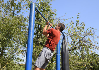 Obraz premium The man pulls himself up on the bar. Playing sports in the fresh air. Homemade Horizontal bar in the backyard.